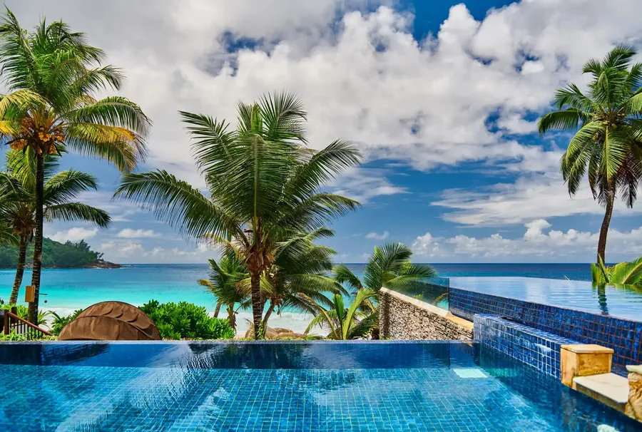 Resort pool among palms and granite boulders above a Seychelles beach