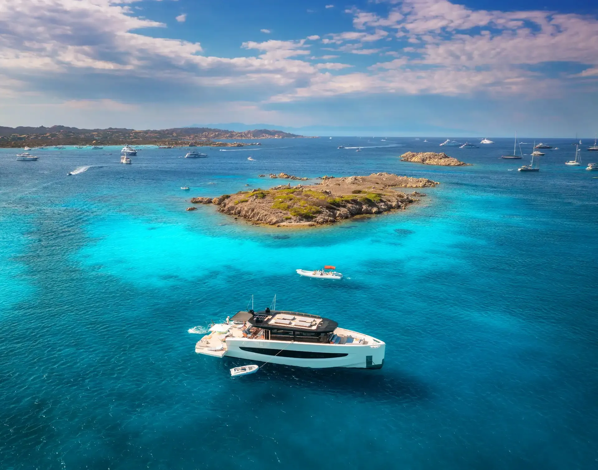 Yacht anchored off a tiny island in clear blue water seen from above