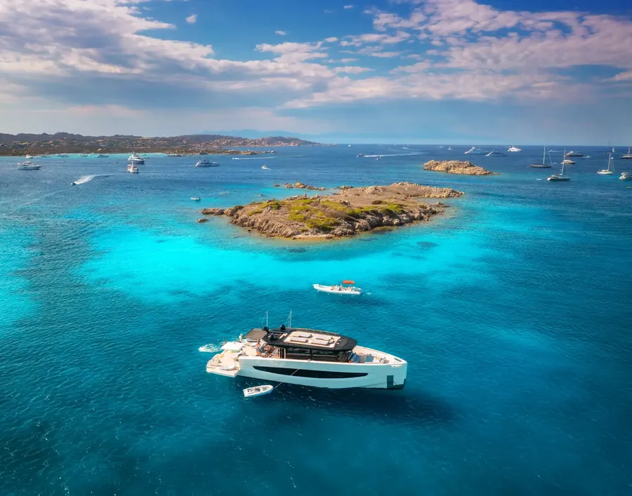 Yacht anchored off a tiny island in clear blue water seen from above