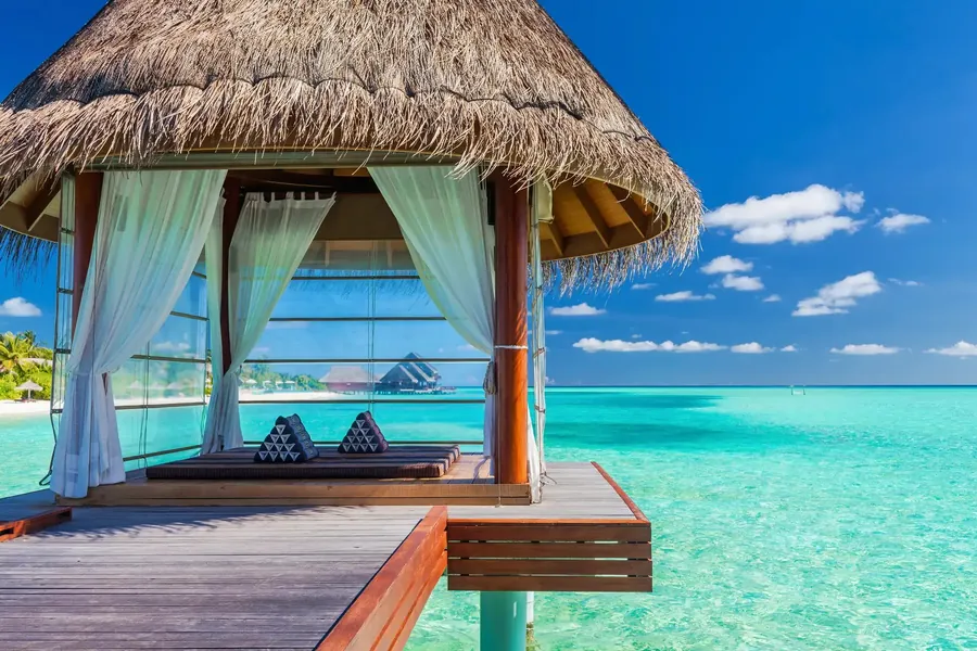 Thatched overwater pavilion with white curtains above a turquoise lagoon